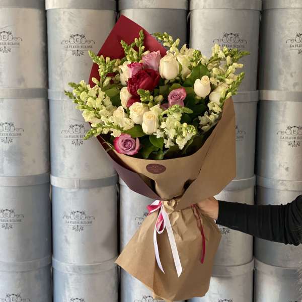 Handheld bouquet of pink, white, and red roses wrapped in brown paper