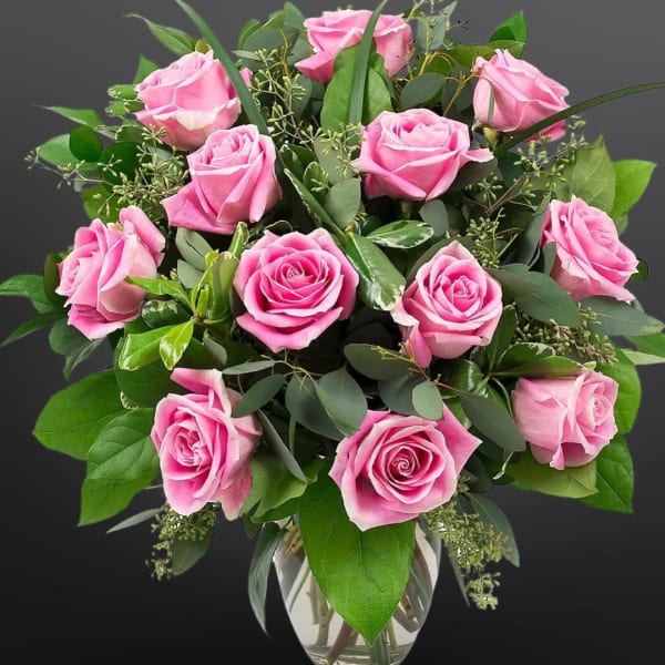 Pink roses arranged in a clear glass vase with greenery