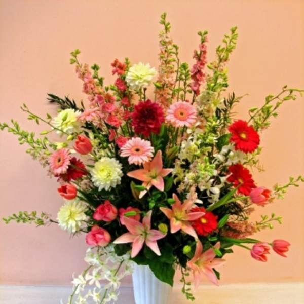 Tall mixed flower arrangement in a white vase with pink, red, and white blooms