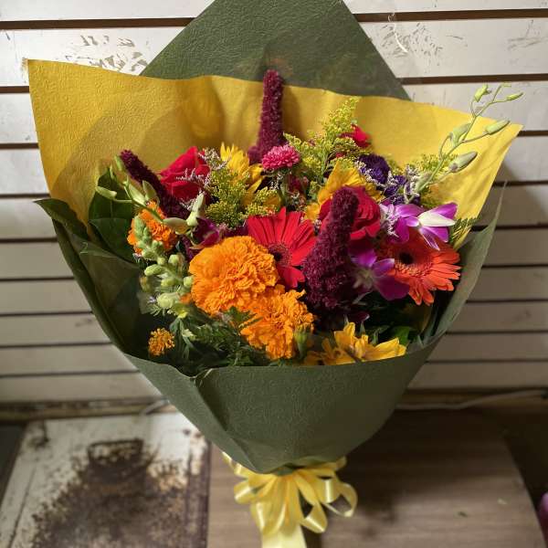 Colorful mixed bouquet wrapped in green and yellow paper with a ribbon