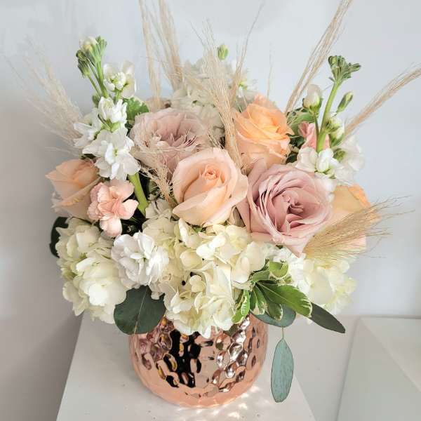 Pastel roses and white hydrangeas in a copper vase with dried grasses