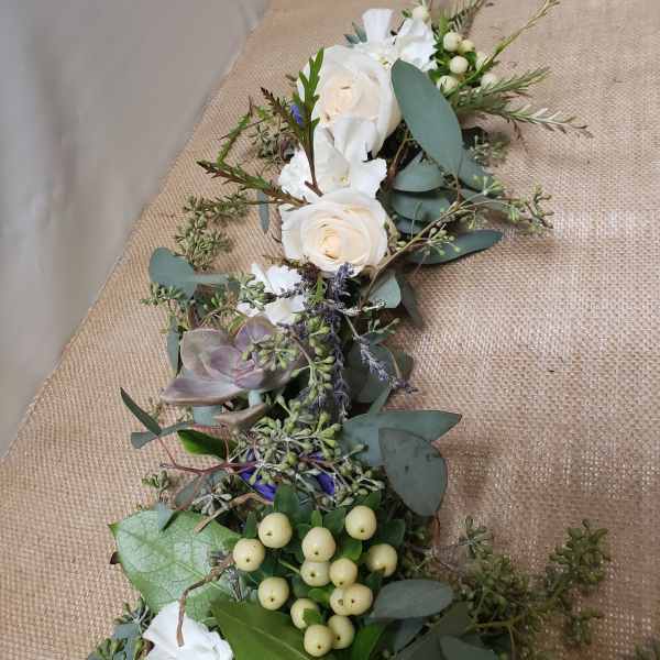 White roses and succulents arranged with eucalyptus and berries on burlap