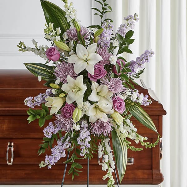 Standing funeral spray with white lilies and lavender flowers on a casket