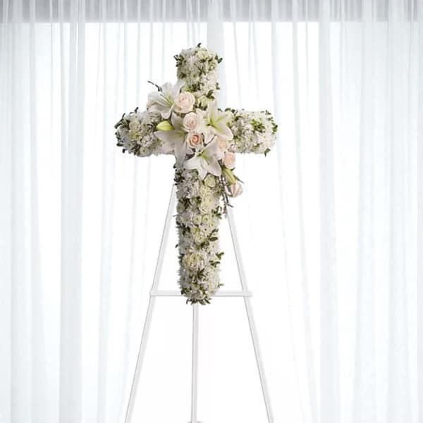 White floral cross arrangement on a stand with roses and lilies