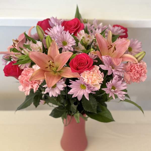 Pink and peach bouquet in a vase with roses, lilies, and daisies