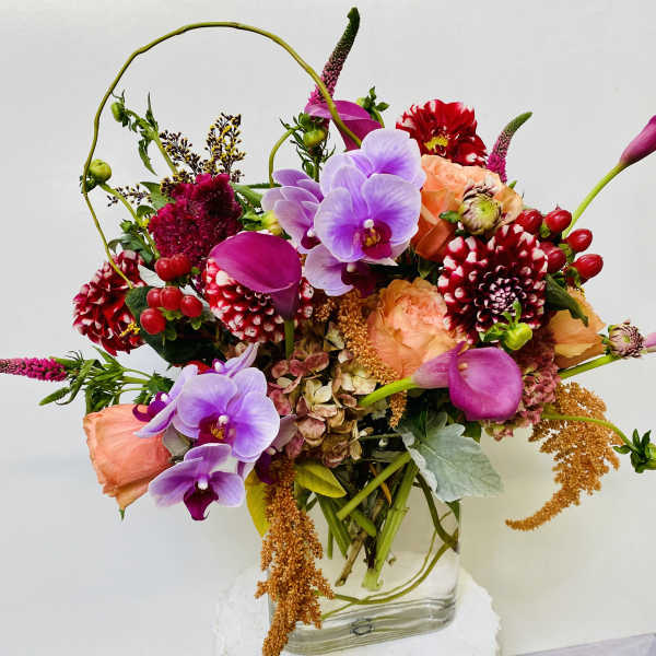 Colorful bouquet with orchids, calla lilies, roses, and dahlias in a glass vase