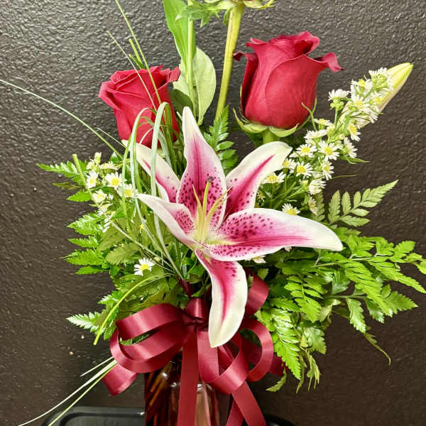 Tall arrangement of red roses and a pink stargazer-style lily in a red glass vase with ribbon