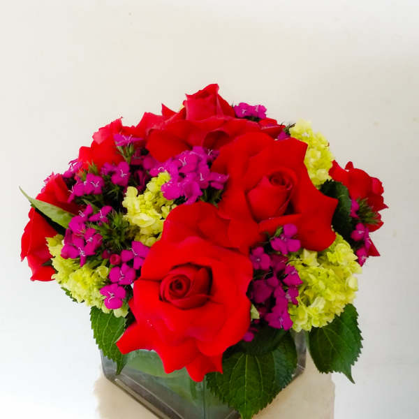 Red roses with pink and yellow filler flowers in a square glass vase