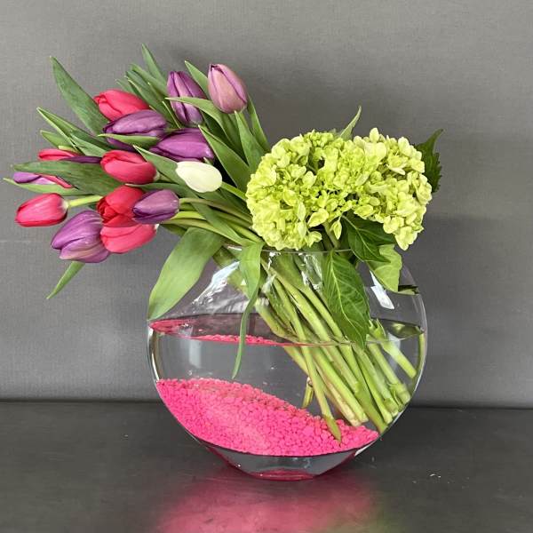 Tulips and green hydrangea in a round glass vase with pink stones