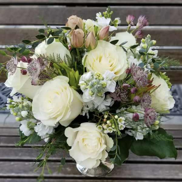 White rose bouquet with small purple flowers in a clear vase