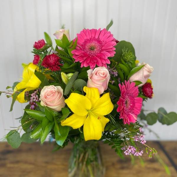 Bouquet of pink gerberas, yellow lilies, and pale roses in a glass vase
