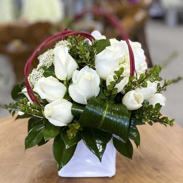 White rose arrangement in a white container with a red handle