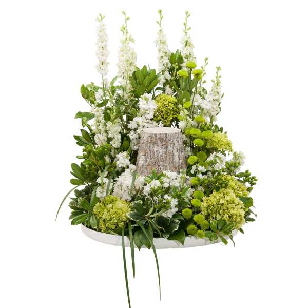Woodland-style arrangement of white and green flowers around a rustic tree-stump accent on a white tray