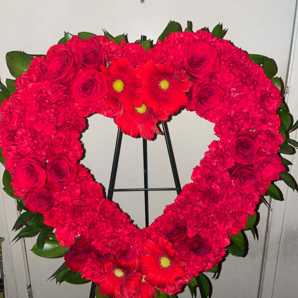Heart-shaped floral wreath of red roses and carnations on a stand