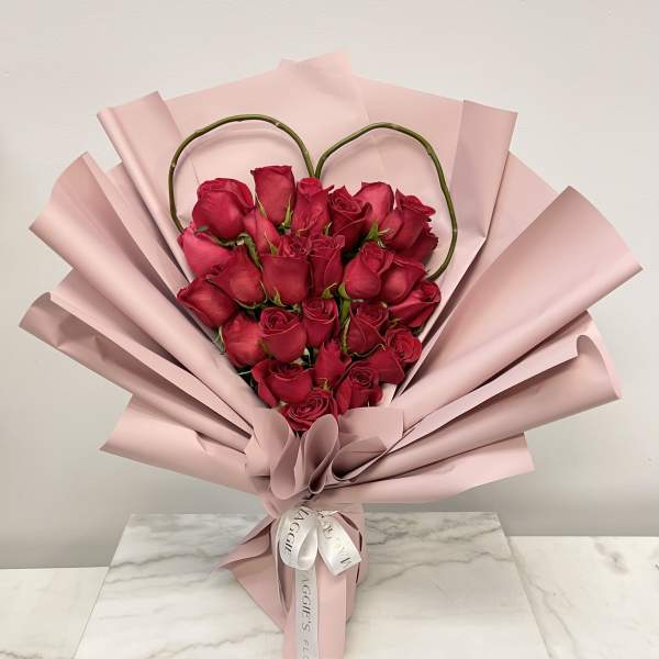 Heart-shaped bouquet of red roses wrapped in pale pink paper