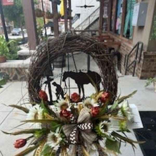Rustic floral arrangement with white blooms and red accents in front of a woven horse sculpture