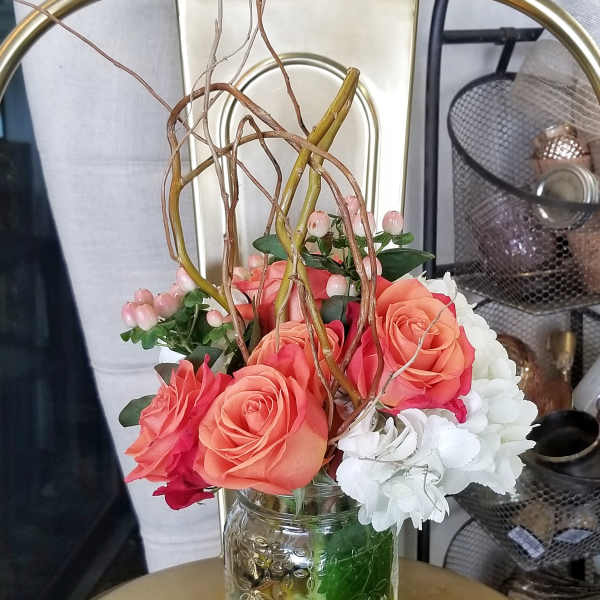 Coral roses and white flowers arranged in a clear glass jar