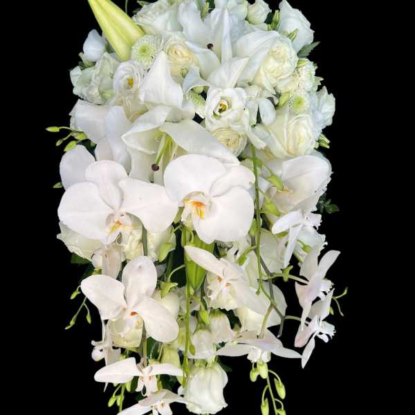 Cascading white bouquet with orchids, lilies, and roses against a black background