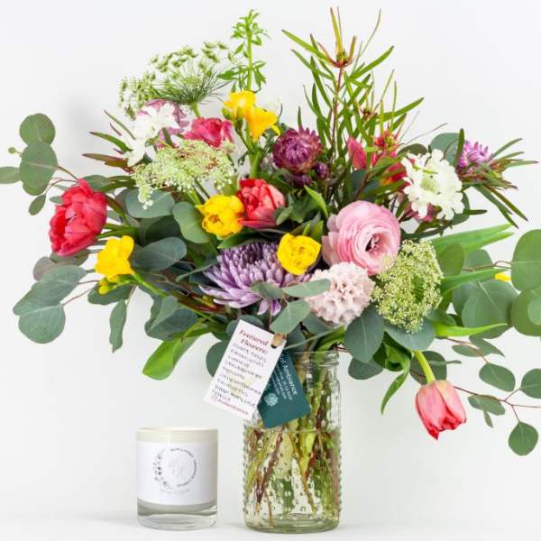 Mixed bouquet in a glass vase with a candle beside it