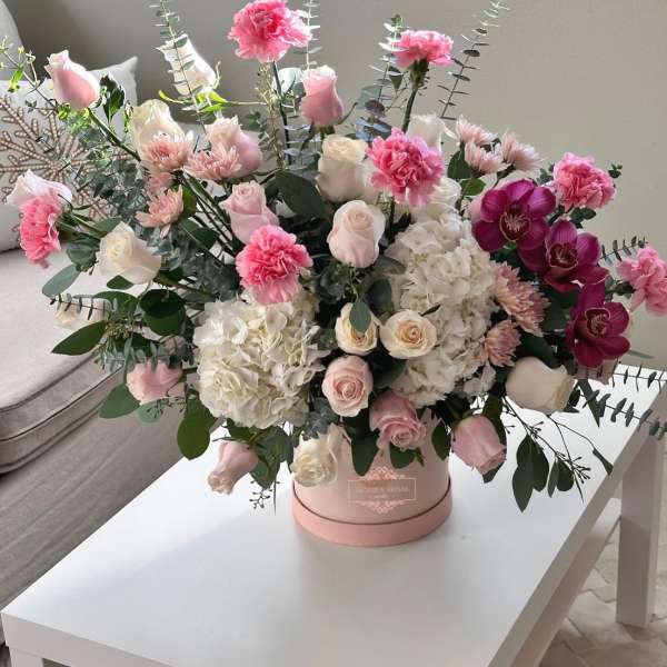 Pink and white roses with hydrangeas and orchids in a round box