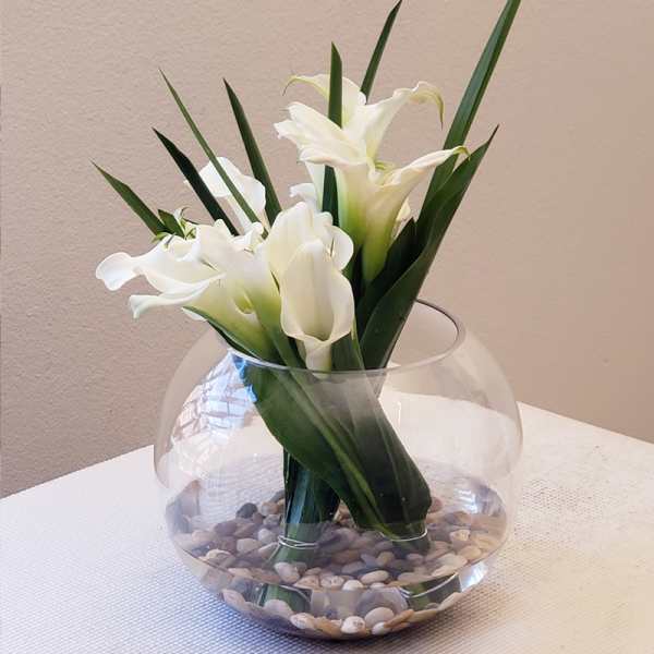 White calla lilies in a round glass vase with pebbles