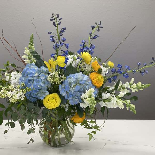 Blue hydrangeas with yellow and white flowers in a glass vase