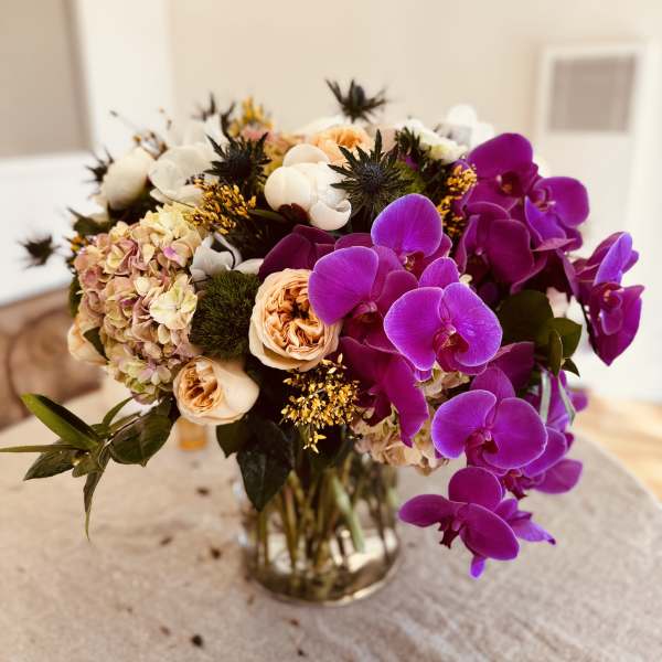 Bouquet of purple orchids, peach roses, and pale hydrangeas in a glass vase