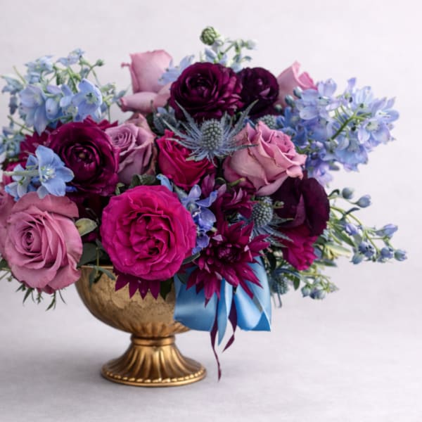 Bouquet of pink and purple roses with blue flowers in a gold vase