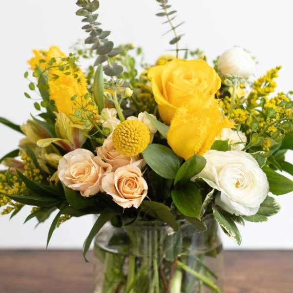 Yellow and cream roses in a glass vase with mixed greenery