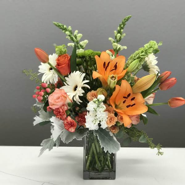 Mixed bouquet with orange lilies, roses, and white daisies in a glass vase