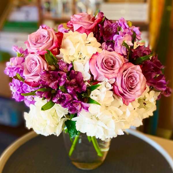 Pink roses and purple flowers arranged with white hydrangeas in a glass vase
