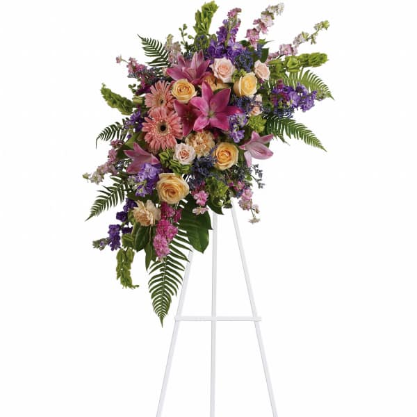 Standing floral spray with pink lilies, roses, and purple blooms on an easel
