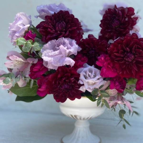 Deep burgundy and lavender flowers arranged in a white pedestal vase