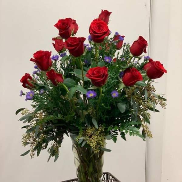 Red roses arranged in a clear glass vase with purple filler flowers