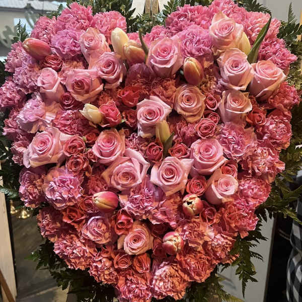 Heart-shaped pink floral arrangement with roses and carnations on an easel