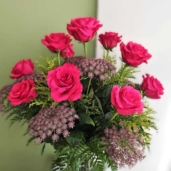 Pink roses arranged in a clear glass vase with purple filler flowers