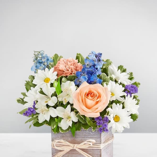 Mixed bouquet with a peach rose, white daisies, and blue flowers in a wooden box