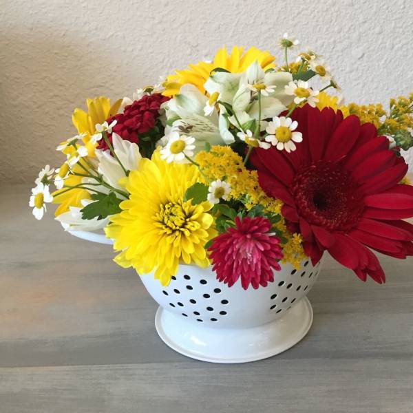 Mixed bouquet of daisies and chrysanthemums in a white colander-style vase
