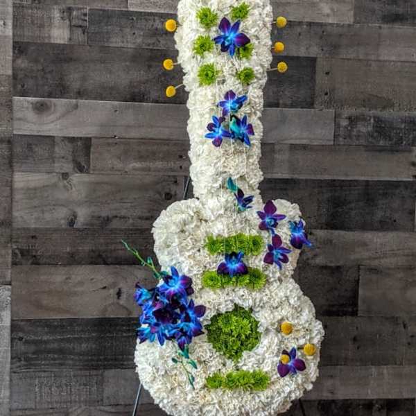 Tall guitar-shaped floral arrangement in white with blue orchids and green accents on a metal stand