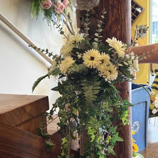 Cream daisy bouquet with trailing ivy and greenery on a wooden post
