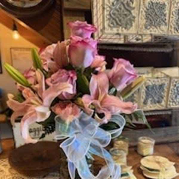 Pink lilies and roses arranged in a vase with a blue ribbon bow