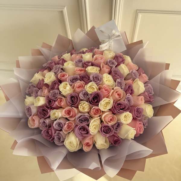 Large bouquet of pink, lavender, and cream roses wrapped in pastel paper