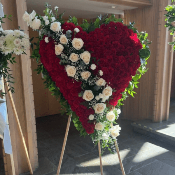 Standing heart-shaped spray of red flowers with white roses on a wooden easel