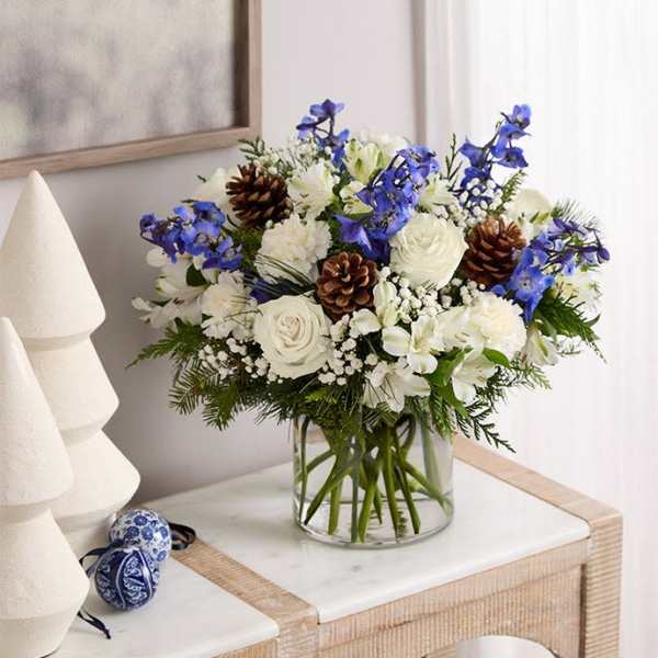 White and blue floral arrangement in a clear glass vase with pinecones