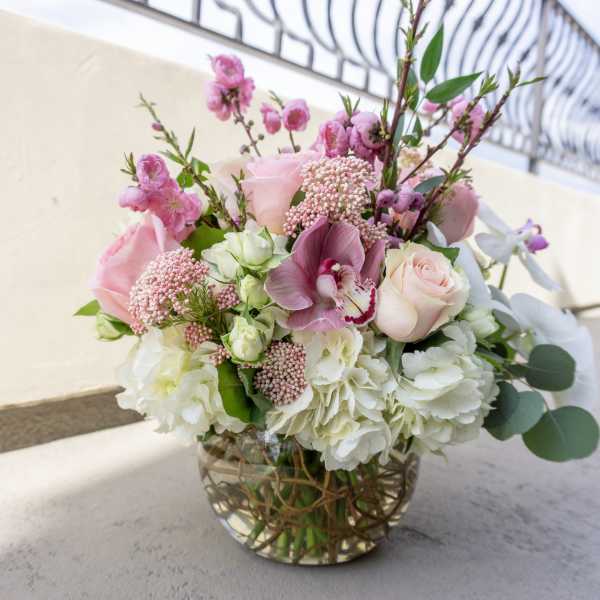 Low round arrangement of pink roses, orchids, and white hydrangeas in a clear glass bowl vase