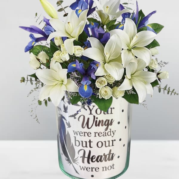 White lilies and blue irises in a glass vase with a memorial message