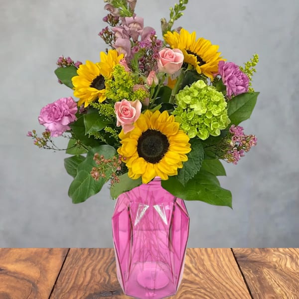 Bouquet of sunflowers, pink roses, and purple flowers in a pink vase