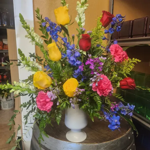 Colorful bouquet of roses, blue flowers, and carnations in a white vase