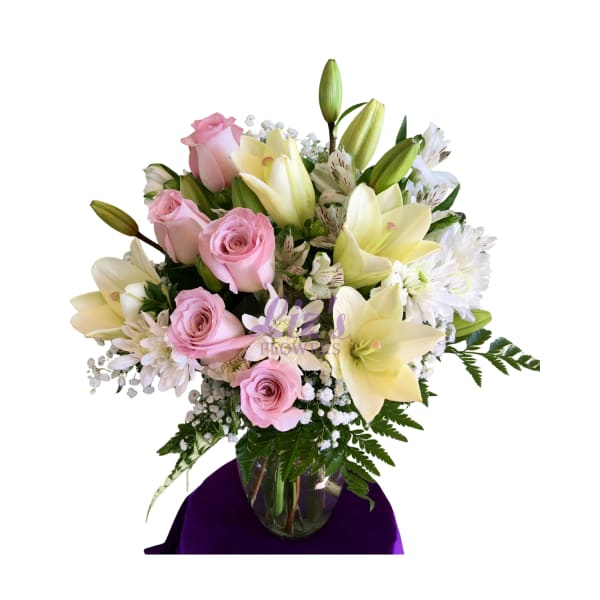 Pink roses and cream lilies with white blooms arranged in a clear glass vase