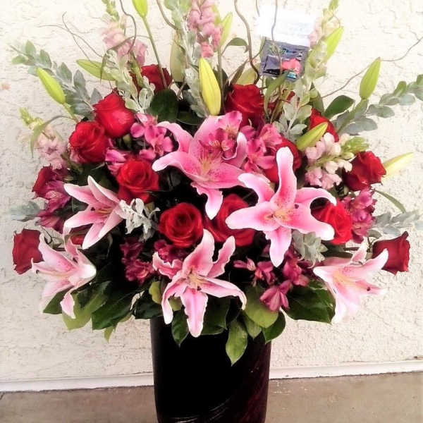 Pink lilies and red roses arranged in a dark vase